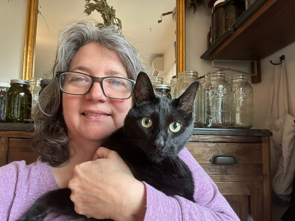 A photo of me--a fierce middle-aged white woman with glasses and gray hair--holding an even fiercer black cat starring straight at the camera 
