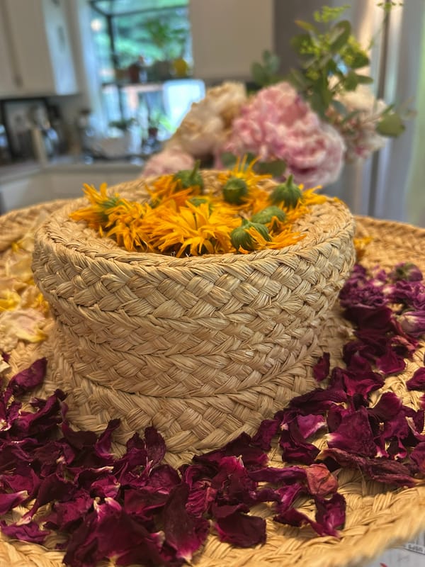 A straw hat holding orange calendula flowers on top and deep pink/purple rose petals around the brim. Drying them.