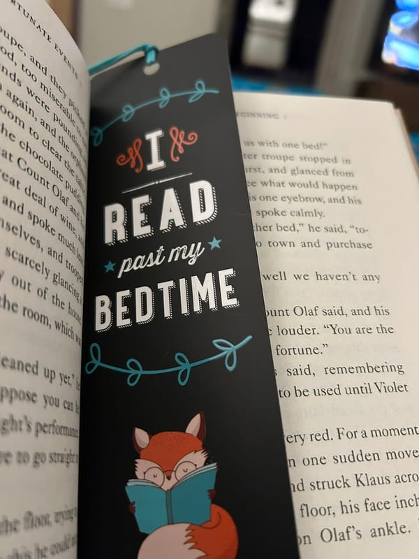 Photo of a bookmark that says "I read past my bedtime" with a cartoon fox, wearing glasses, with her nose in a book